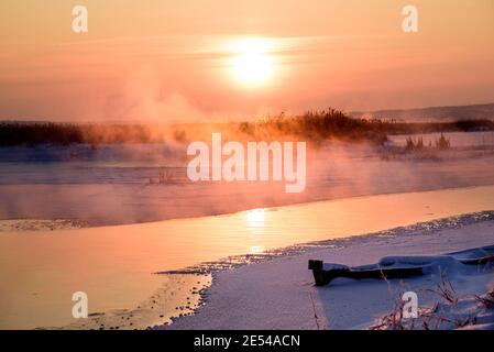 Paysage d'hiver, brume et brouillard se levant de l'eau libre d'une rivière en streaming, gelé, neigeux, gelé fleuve Narew en Pologne pendant un lever de soleil froid Banque D'Images