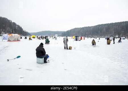 Pêcheur pêchant sur un lac gelé en hiver avec un poteau ou une canne à pêche, une tarière à glace et de l'équipement pour la pêche Banque D'Images