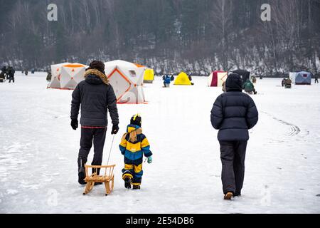 Famille avec enfant ou enfant marchant sur un lac gelé en hiver avec des pêcheurs sur fond Banque D'Images