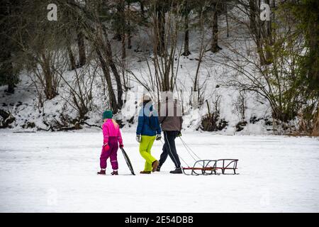 Famille avec enfant ou enfant marchant sur un lac gelé en hiver, avec traîneau et forêt en arrière-plan Banque D'Images