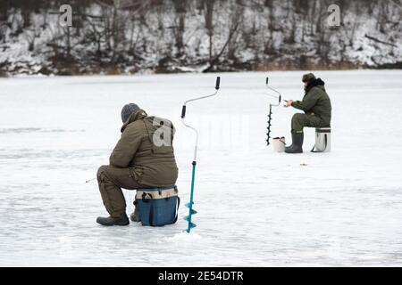 Pêcheurs pêchant sur un lac gelé en hiver avec un poteau ou une canne à pêche, une tarière à glace et du matériel de pêche Banque D'Images