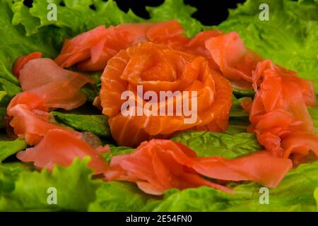 Syake sashimi avec des tranches de saumon disposées sous forme de rose, de citron, de wasabi et de feuilles de laitue sur une assiette rectangulaire, en gros plan. Banque D'Images