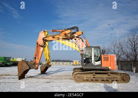 puissantes pelles hydrauliques sur chenilles orange et jaune sur un chantier de construction. Location, location de terrassement. Neige, hiver, ensoleillé Banque D'Images