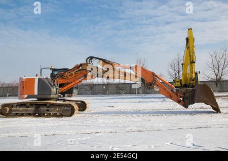 Deux grandes pelles sur chenilles sont stationnée sur un chantier de construction. Une puissante pelle hydraulique orange au premier plan avec une flèche au-dessus de la neige-c Banque D'Images