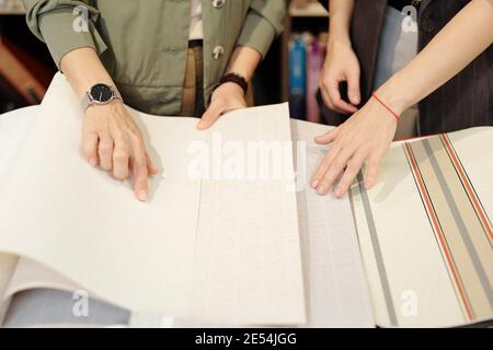 Les mains de la jeune assistante de boutique aidant le client à choisir nouveaux papiers peints en studio de design intérieur tout en pointant vers l'un des échantillons Banque D'Images