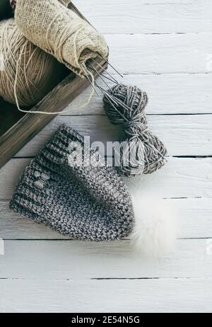 Bonnet style wainter en maille avec pompon moelleux et fil gris laine sur fond de bois blanc. Banque D'Images