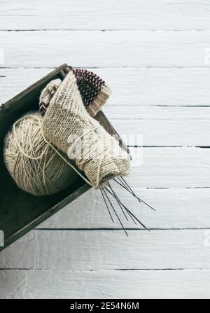 Boule de fils de laine rugueux et aiguilles de tricotage dans une boîte sur fond de planches en bois blanc. Banque D'Images