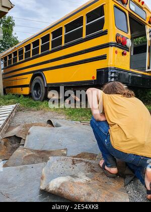 Photo grand angle d'un jeune homme s'agenouillant au milieu des matériaux de charpentier utilisés pour rénover et donner vie à un vieux bus. Banque D'Images