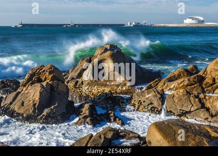 Smashing vagues contre des rochers sur la plage à Nevogilde paroisse civile de Porto, au Portugal. Port de Leixoes Cruise Terminal building on background Banque D'Images