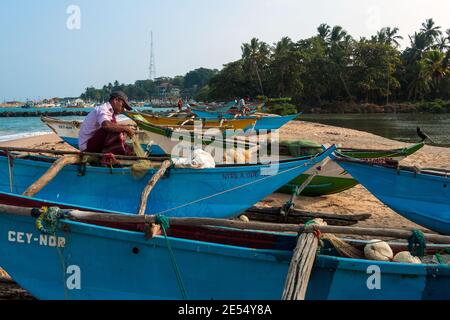 Tangalle, Sri Lanka: Les pêcheurs réparent les filets sur les bateaux qui sont sur la plage de la ville Banque D'Images