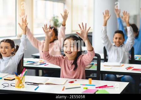 Divers petits écoliers levant les mains en classe Banque D'Images