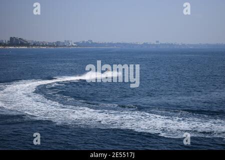 Jeune homme dans un gilet de sauvetage à bord d'un scooter des eaux blanc et bleu sur la haute mer bleue, formant de grandes vagues, des éclaboussures et de la mousse sur le fond clair sk Banque D'Images