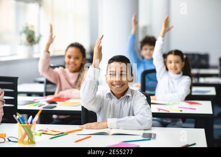 Divers petits écoliers levant les mains en classe Banque D'Images