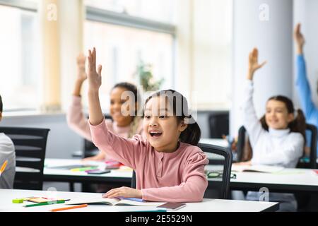 Divers petits écoliers levant les mains en classe Banque D'Images