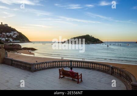 Donostia, Gipuzkoa, pays Basque, Espagne - 12 juillet 2019 : les gens s'assoient sur un banc pour admirer le coucher du soleil sur la plage de la Concha. Banque D'Images