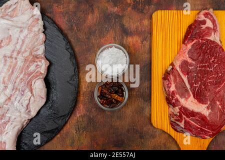 Steak de bœuf cru et secret de porc sur un plateau de cuisine en bois et plaque d'ardoise ronde sur une ancienne table en bois dans des tons bruns. Concept gastronomique Banque D'Images