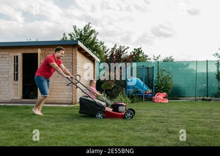 Père et son fils tondent la pelouse ensemble. Longueur complète d'un jeune garçon coupant l'herbe avec son père. Banque D'Images