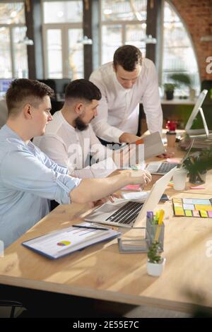 Concentré, attenté. De jeunes collègues du caucase travaillent ensemble dans un bureau utilisant des appareils et des gadgets modernes. L'air occupé, attenté, joyeux, réussi. Concept d'entreprise, de bureau, de finances. Banque D'Images