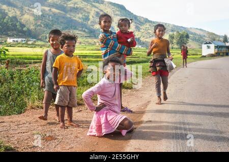 Manandoana, Madagascar - 26 avril 2019: Groupe d'enfants malgaches inconnus jouant sur la route à côté du champ de riz, de petites collines en arrière-plan, des gens à Madag Banque D'Images