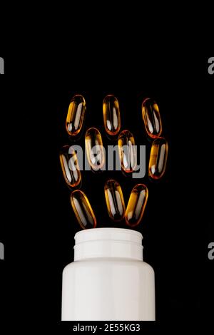 Capsules Omega-3 sur fond noir. Concept de santé avec capsules d'huile de poisson. Bouteille blanche Banque D'Images