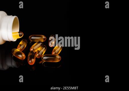Capsules Omega-3 sur fond noir. Concept de santé avec capsules d'huile de poisson. Bouteille blanche Banque D'Images