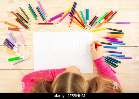 La petite fille se prépare à peindre sur une feuille de papier vierge. Le dessin est fait par un enfant avec des crayons de couleur ou des stylos-feutres. Dessin des enfants. Voir fr Banque D'Images