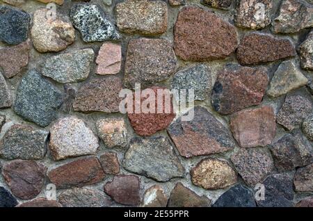 Fragment texturé de la façade relief d'un mur en pierre de granit granuleux de teintes marron, grise, beige et marron, fixé avec du ciment gris Banque D'Images