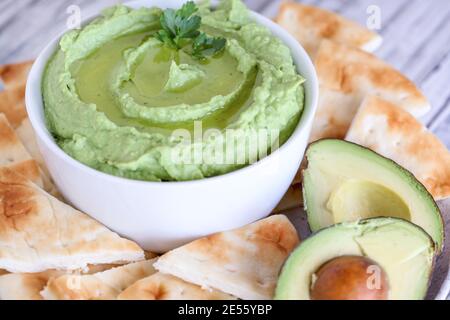 Bogan avocat Hummus, fait avec des pois chiches, des avocats et des tahini, avec de l'huile d'olive. Garnie de persil et servie avec du pain pita sur une table rustique. Banque D'Images