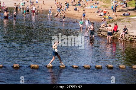 Une jeune femme qui tente de négocier les pierres glissantes sur la rivière à côté des terrains de l'abbaye de Bolton. Banque D'Images