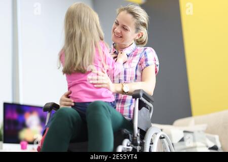 Une femme souriante en fauteuil roulant embrasse une petite fille Banque D'Images