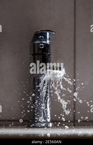 Robinet d'eau cassé dans le lavabo de la salle de bains. Projections d'eau du robinet argenté Banque D'Images