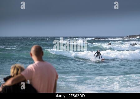 Vacanciers observant un surfeur solitaire qui fait une vague près des rochers à Fistral, à Newquay, dans les Cornouailles.