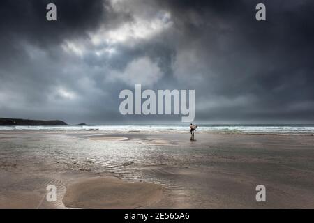 Un surfeur d'exécution de la mer portant sa planche de surf comme une sombre tempête spectaculaire plage de Fistral approches à Newquay en Cornouailles. Banque D'Images