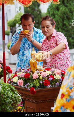 Deux personnes versent de l'eau sur une statue de Bouddha pendant Songkran, nouvel an thaïlandais, à Bangkok, en Thaïlande. Banque D'Images