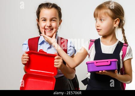 Élèves de l'école primaire avec des boîtes à lunch entre les mains. Les filles avec des sacs à dos mangent des fruits. Début des leçons. Premier jour de l'automne. Banque D'Images