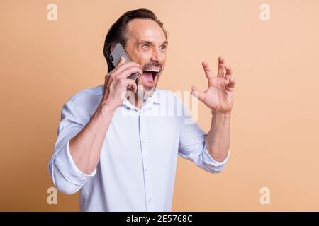 Photo de profil de l'homme fou en colère tenir téléphone cri look vide espace porter chemise isolé beige couleur fond Banque D'Images