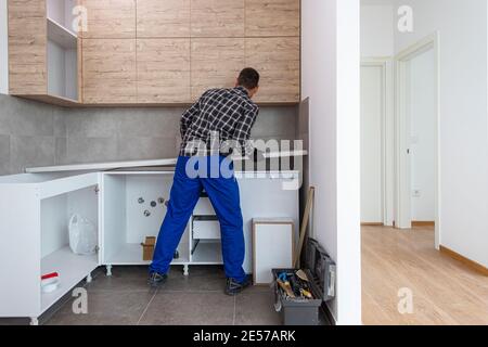 Le menuisier met la surface de travail de la cuisine en place, dans la cuisine presque finie avec les éléments suspendus sur le mur. Banque D'Images