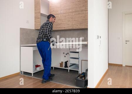 Le menuisier met la surface de travail de la cuisine en place, dans la cuisine presque finie avec les éléments suspendus sur le mur. Banque D'Images