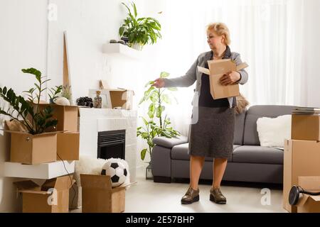 Heureuse excitée mature retraité d'âge moyen femme debout dans moderne l'intérieur du salon seul avec les bras étirés jouissent de la liberté et sensation de bien-être Banque D'Images