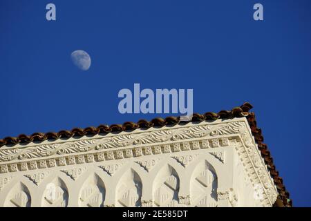 Lune de jour, lune blanche, demi-lune, contre un ciel bleu, suspendue au-dessus d'un toit en forme de chiglé. Oakland, Californie Banque D'Images