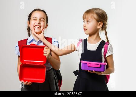 Élèves de l'école primaire avec des boîtes à lunch entre les mains. Les filles avec des sacs à dos mangent des fruits. Début des leçons. Premier jour de l'automne. Banque D'Images