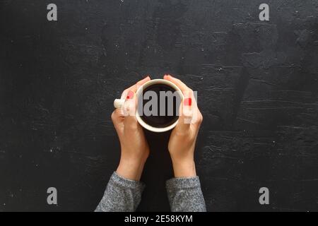 Les mains des femmes tenant des tasses de café sur fond de table rustique en bois, les mains de la femme dans le chandail tiennent une tasse de café fort sur table en bois. Café f Banque D'Images