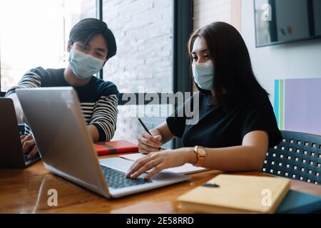 Femmes et hommes asiatiques se rencontrent avec un ordinateur portable pour les masques financiers et de protection empêchent le virus corona ou covid19 dans l'espace de travail commun Banque D'Images