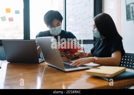 Femmes et hommes asiatiques se rencontrent avec un ordinateur portable pour les masques financiers et de protection empêchent le virus corona ou covid19 dans l'espace de travail commun Banque D'Images