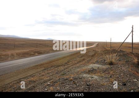 Une route asphaltée traversant la steppe du matin le long de la ligne électrique. Chuya steppe, Altaï, Sibérie, Russie. Banque D'Images