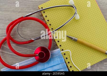 Thème médical encore la vie avec un stéthoscope rouge coloré et masque chirurgical placé sur le côté du fil relié le bloc-notes et le stylet sont considérés comme une pose à plat Banque D'Images