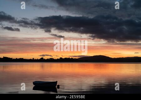 Silhouette de petit canot pneumatique dans la baie avec lumière orange de l'heure d'or réfléchie à Tauranga en Nouvelle-Zélande. Banque D'Images