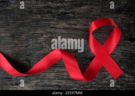 Vue de dessus du ruban rouge sur fond de bois sombre vieilli. Concept de sensibilisation au sida, au VIH, aux maladies cardiaques et aux accidents vasculaires cérébraux. Dépistage du VIH et du sida. Banque D'Images