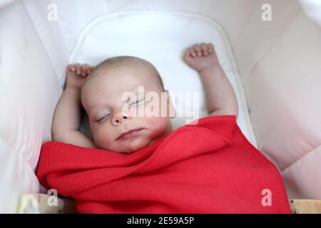 Bébé dormant sous une couverture rouge dans le lit Banque D'Images