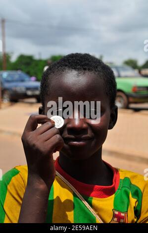 Un garçon burkinabé qui détient une pièce de 100 francs d'Afrique de l'Ouest. Banque D'Images